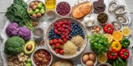 Top-down flat lay view of hormone-balancing foods including broccoli, kale, wild-caught salmon, avocado, blueberries, and walnuts arranged neatly on a white rustic wooden table.