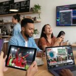 Realistic scene of diverse people in a modern cafe looking at smartphones and laptops displaying 2025 viral trends, including AI avatars, sports highlights, and social media glitches.